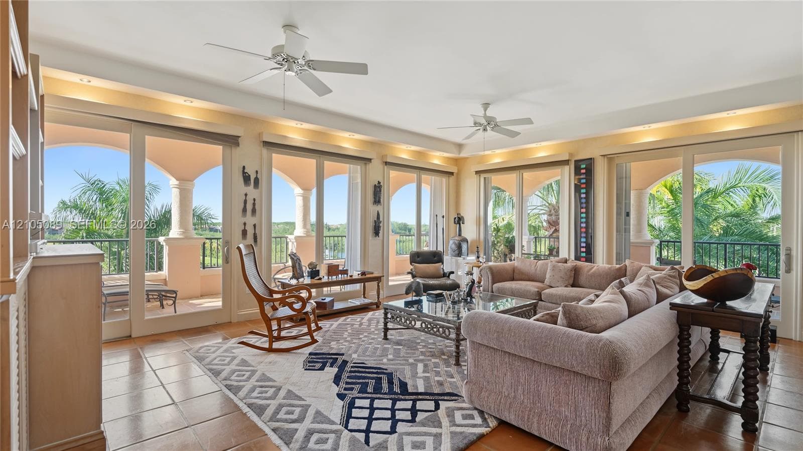 Living area featuring large format tile flooring, crown molding with recessed lighting, dual ceiling fans, and expansive sliding glass doors opening to a covered balcony