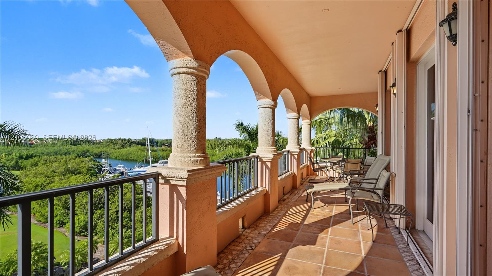Covered terrace featuring arched masonry columns, terracotta tile flooring, metal railings, and integrated wall-mounted lighting