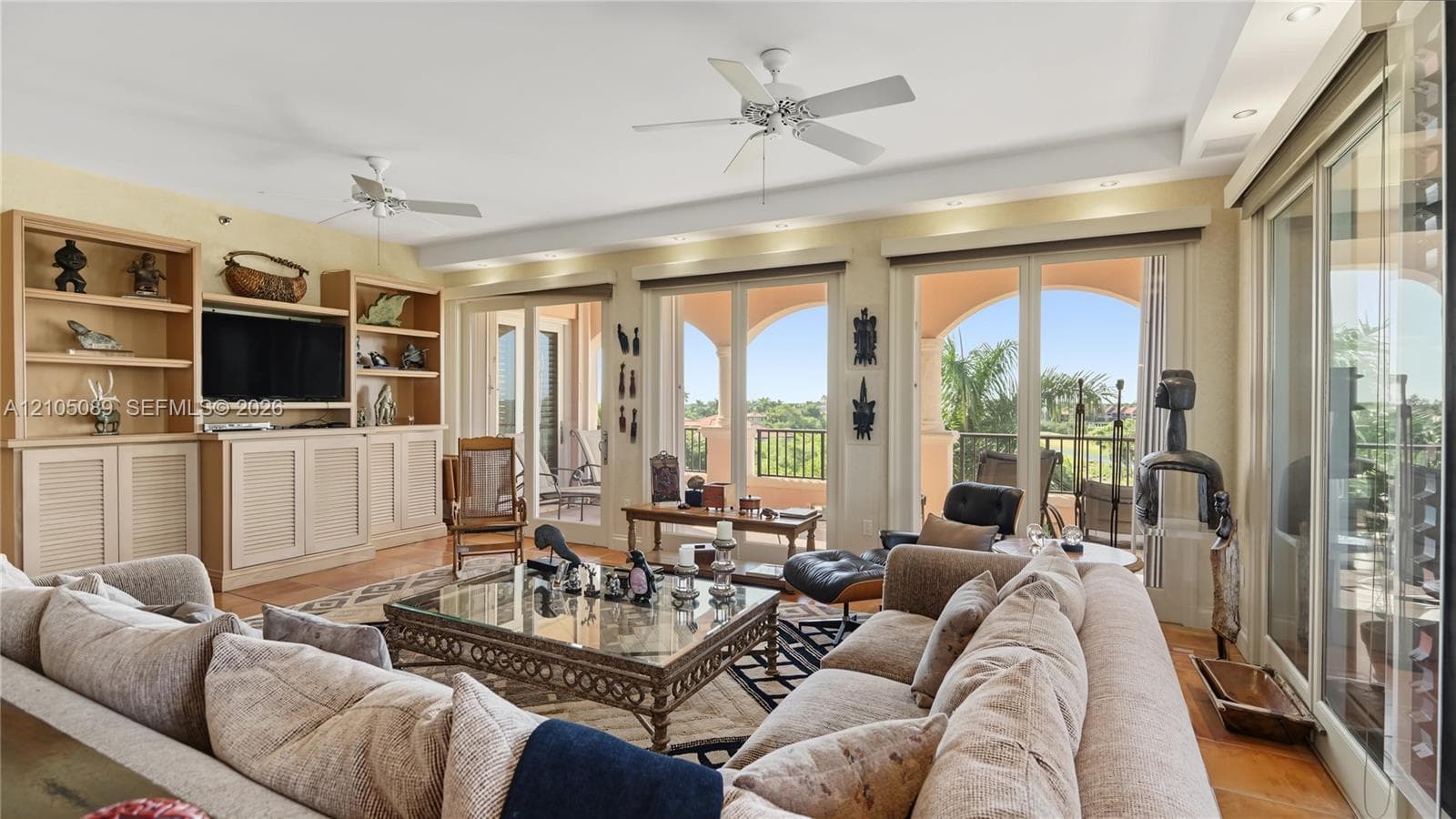 Spacious living area featuring custom built-in cabinetry, tray ceilings with dual overhead fans, recessed lighting, and expansive multi-panel sliding glass doors