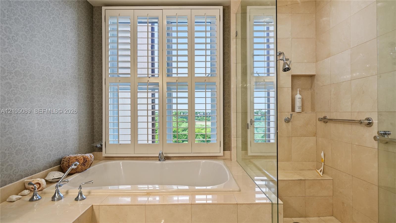 Built-in soaking tub with tile surround, glass-enclosed shower with recessed shelving, and plantation shutters