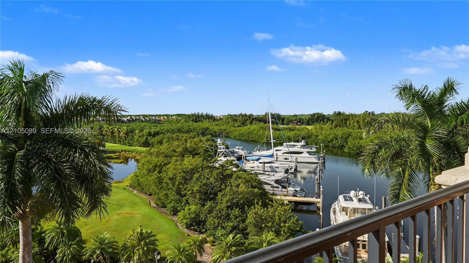 Balcony with metal railing overlooking a waterway, marina with private boat slips, palm trees, and dense foliage