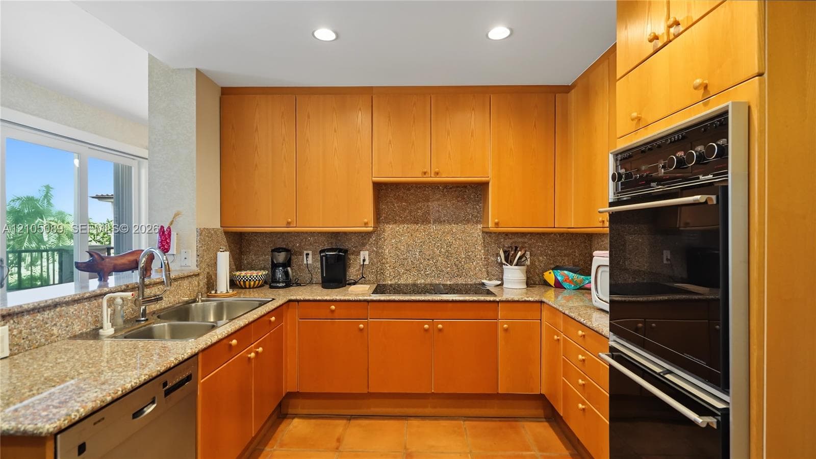 Kitchen featuring natural wood cabinetry, stone-surface countertops, dual-basin stainless steel sink with a high-arch faucet, built-in electric wall oven, and integrated cooktop