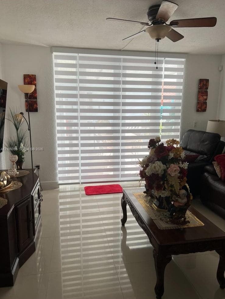 Large sliding glass door featuring adjustable horizontal blinds, light-colored tile flooring, and a ceiling-mounted light fixture with a fan
