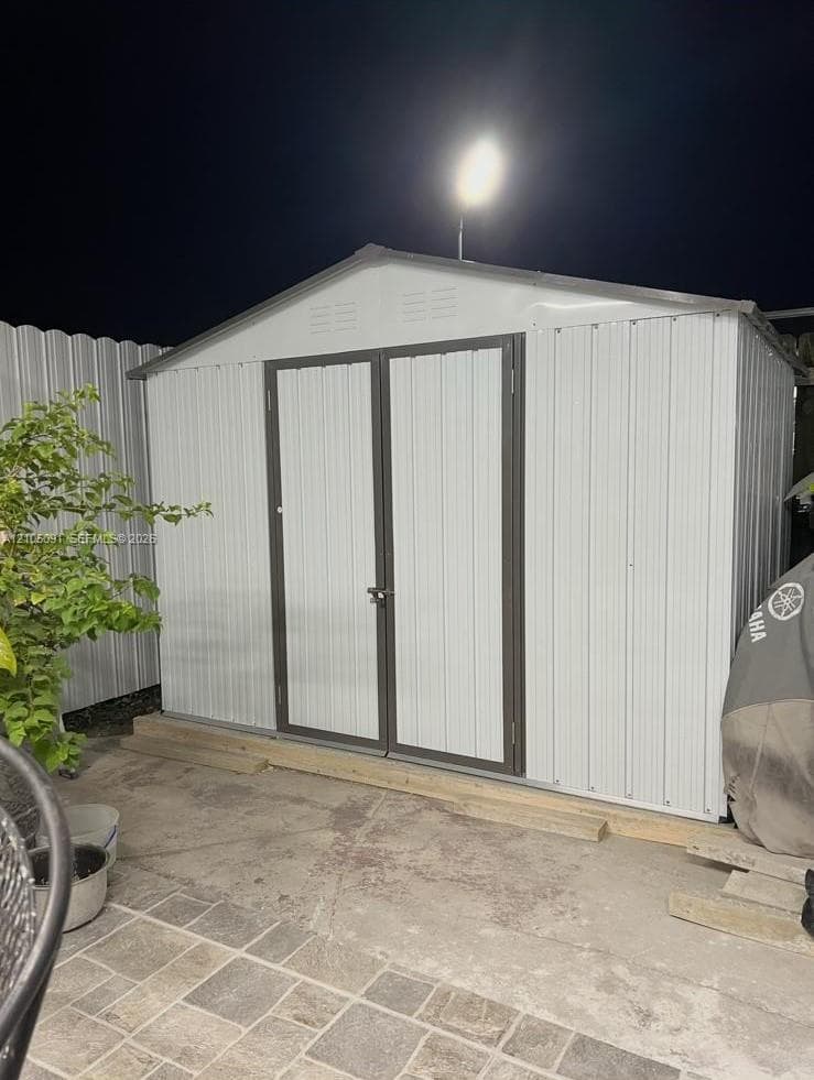Gable-roof storage structure featuring metal panel siding, double-door entry, and a concrete foundation