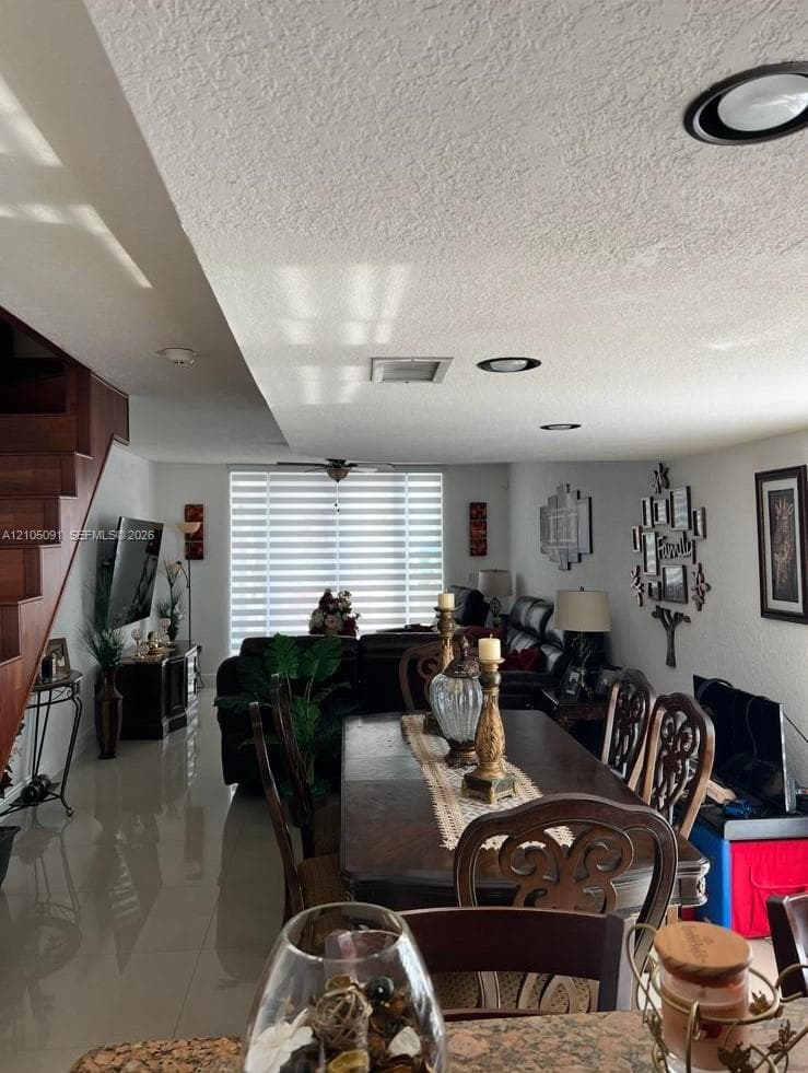 Open-concept floor plan featuring polished tile flooring, recessed ceiling lighting, horizontal window blinds, and a wood-finish staircase