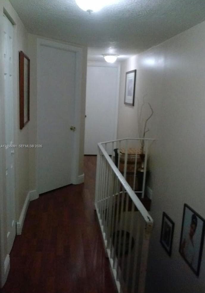 Hallway featuring wood-finish flooring, white paneled doors, and a metal stair railing
