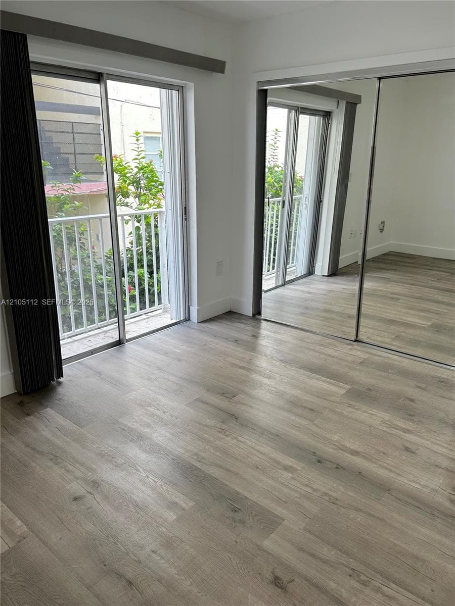 Wood-finish flooring, sliding glass door with balcony access, and mirrored closet doors
