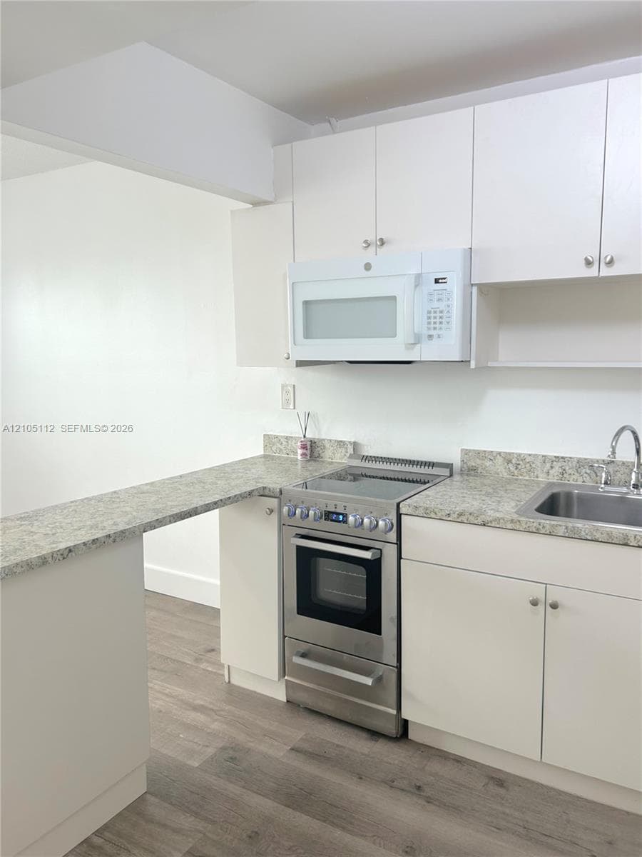 Kitchen featuring white cabinetry, stone-finish countertops, stainless steel electric range, over-the-range microwave, and wood-finish flooring