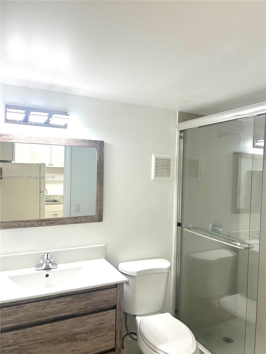 Bathroom featuring a wood-finish vanity with a rectangular basin, framed wall mirror, three-light vanity fixture, and a glass-enclosed shower