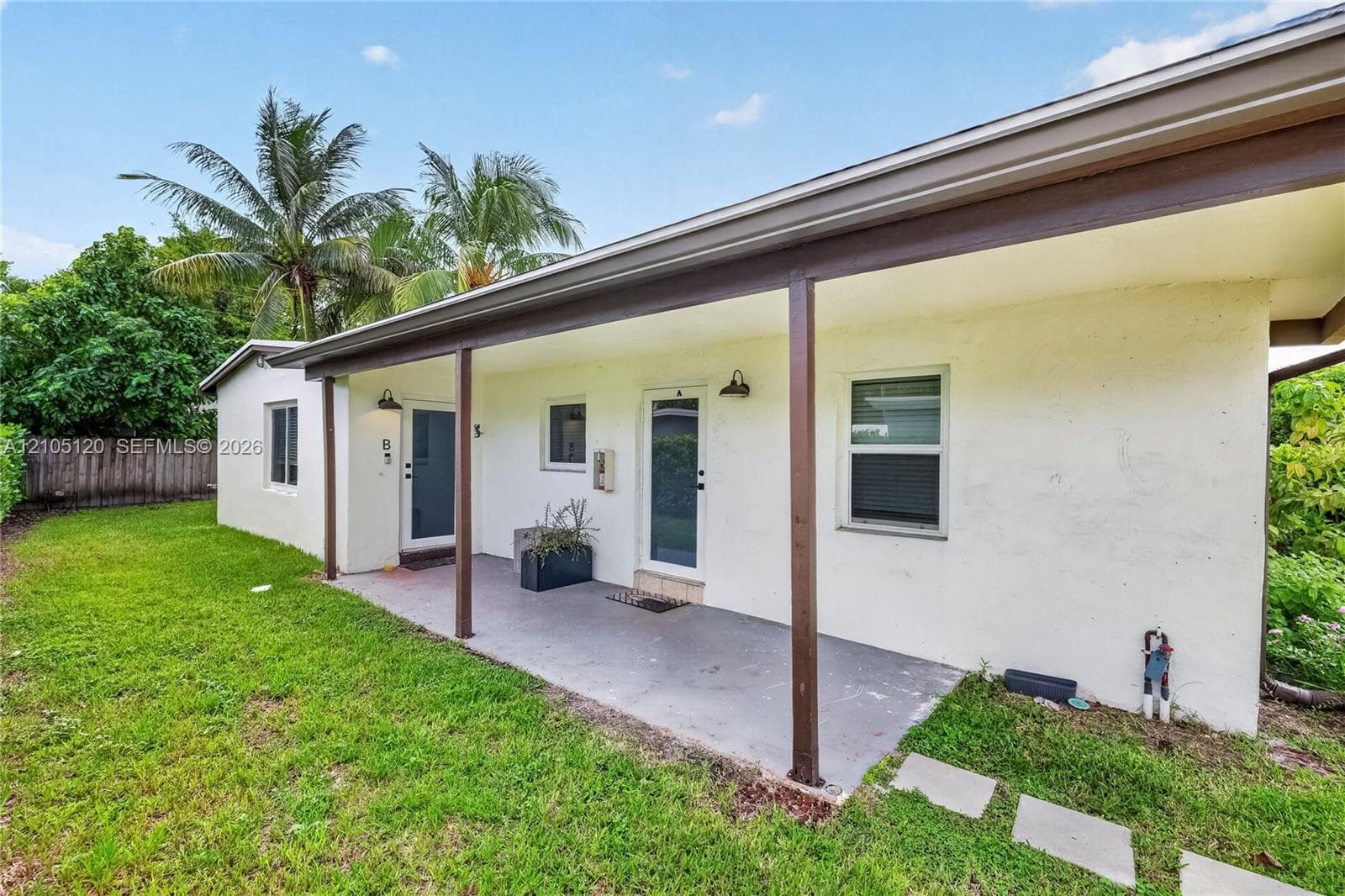 Covered patio featuring concrete flooring, structural support columns, dual exterior doors, and exterior wall-mounted lighting