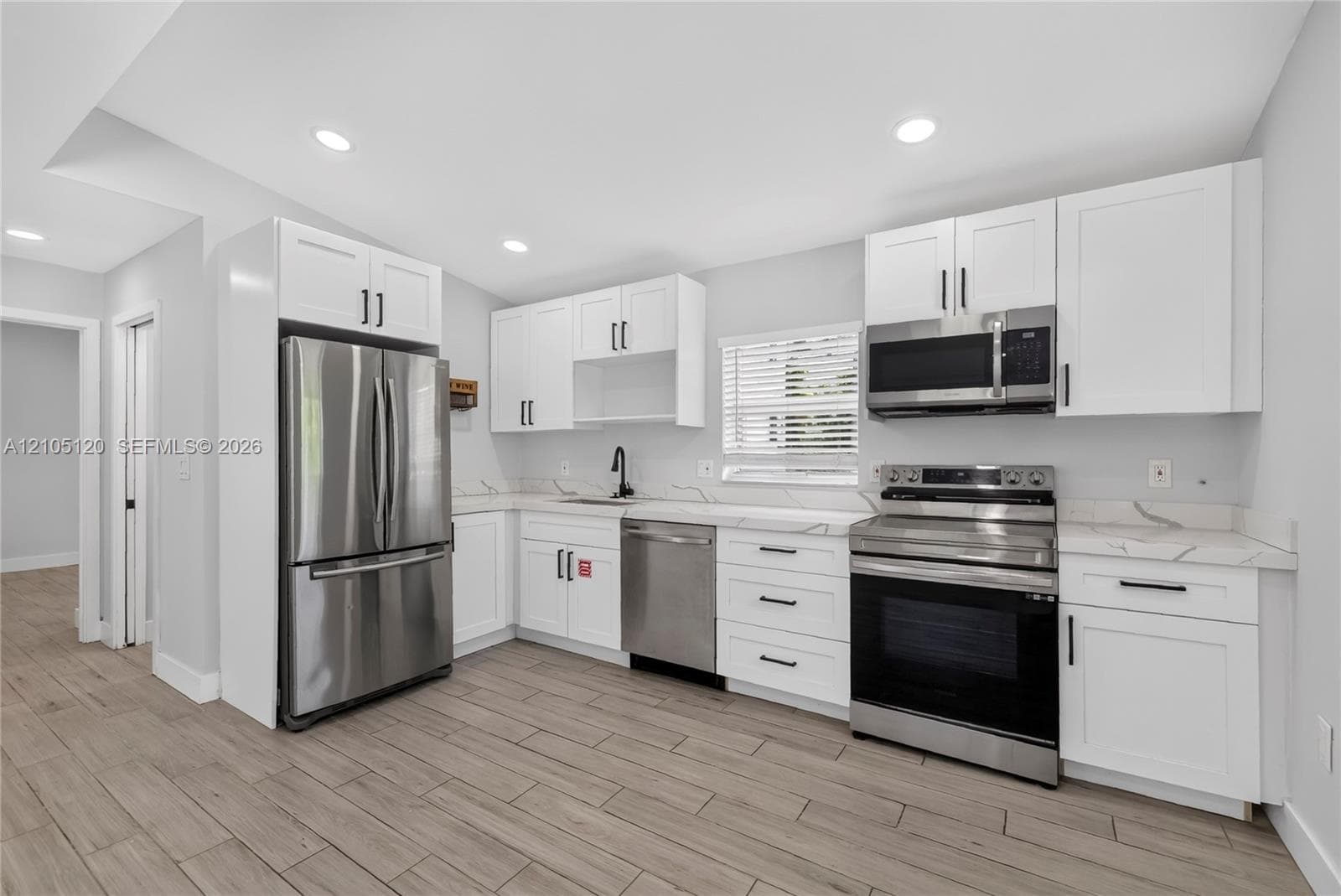 Kitchen featuring white shaker cabinetry, stainless steel appliances, stone-patterned countertops, recessed lighting, and wood-finish flooring