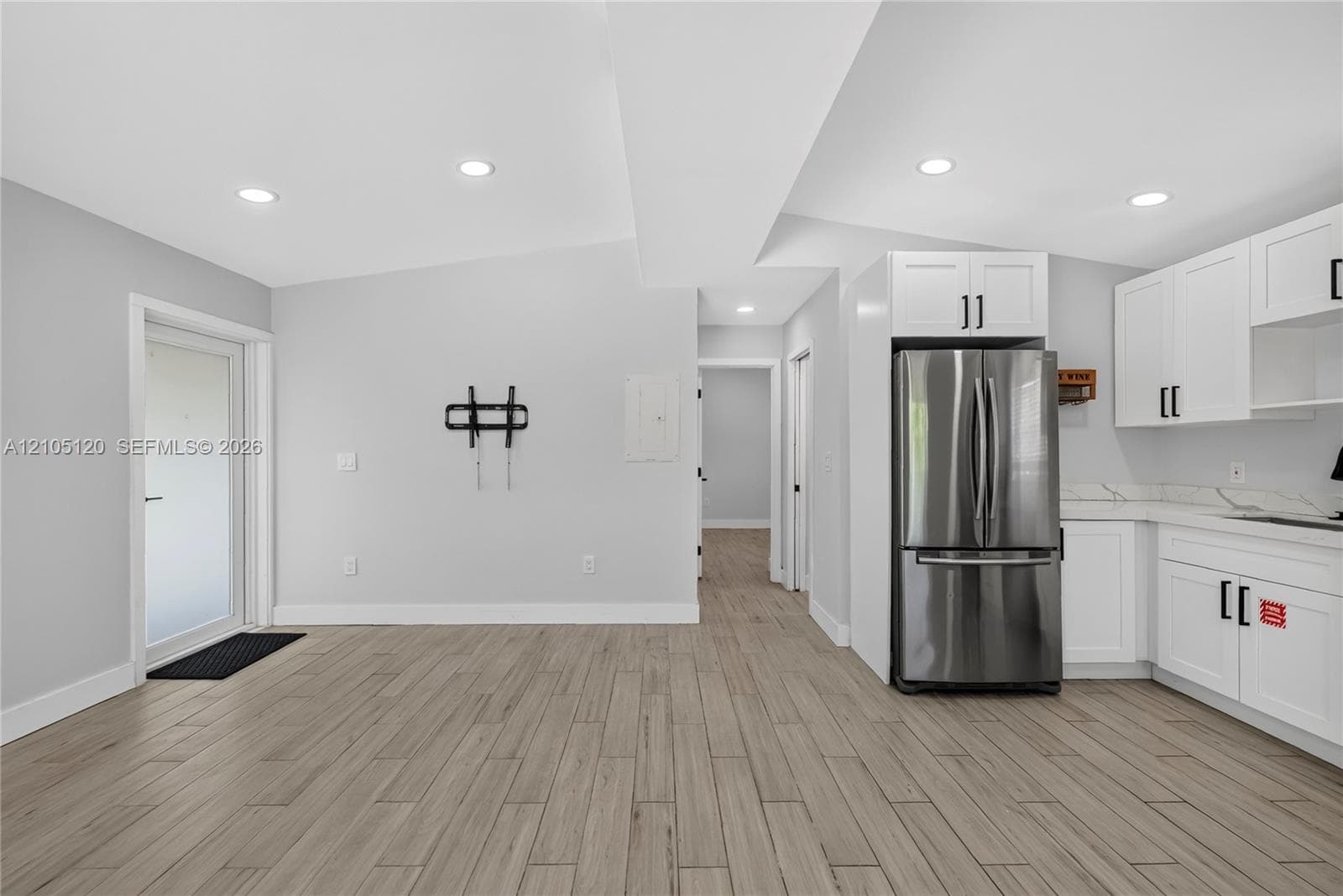 Wood-finish flooring, white shaker-style cabinetry, stainless steel refrigerator, stone-style countertops, and recessed lighting