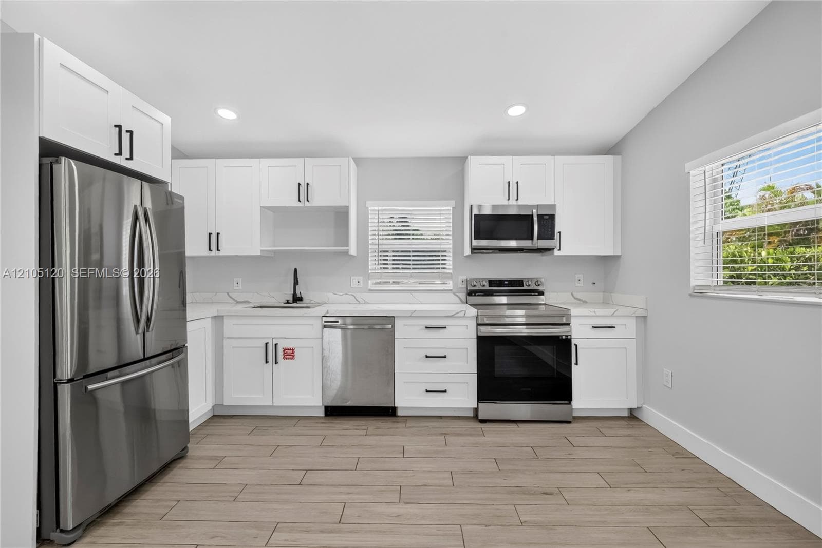 Kitchen featuring white Shaker-style cabinetry, stainless steel appliances, light-toned stone-finish countertops, and wood-finish flooring