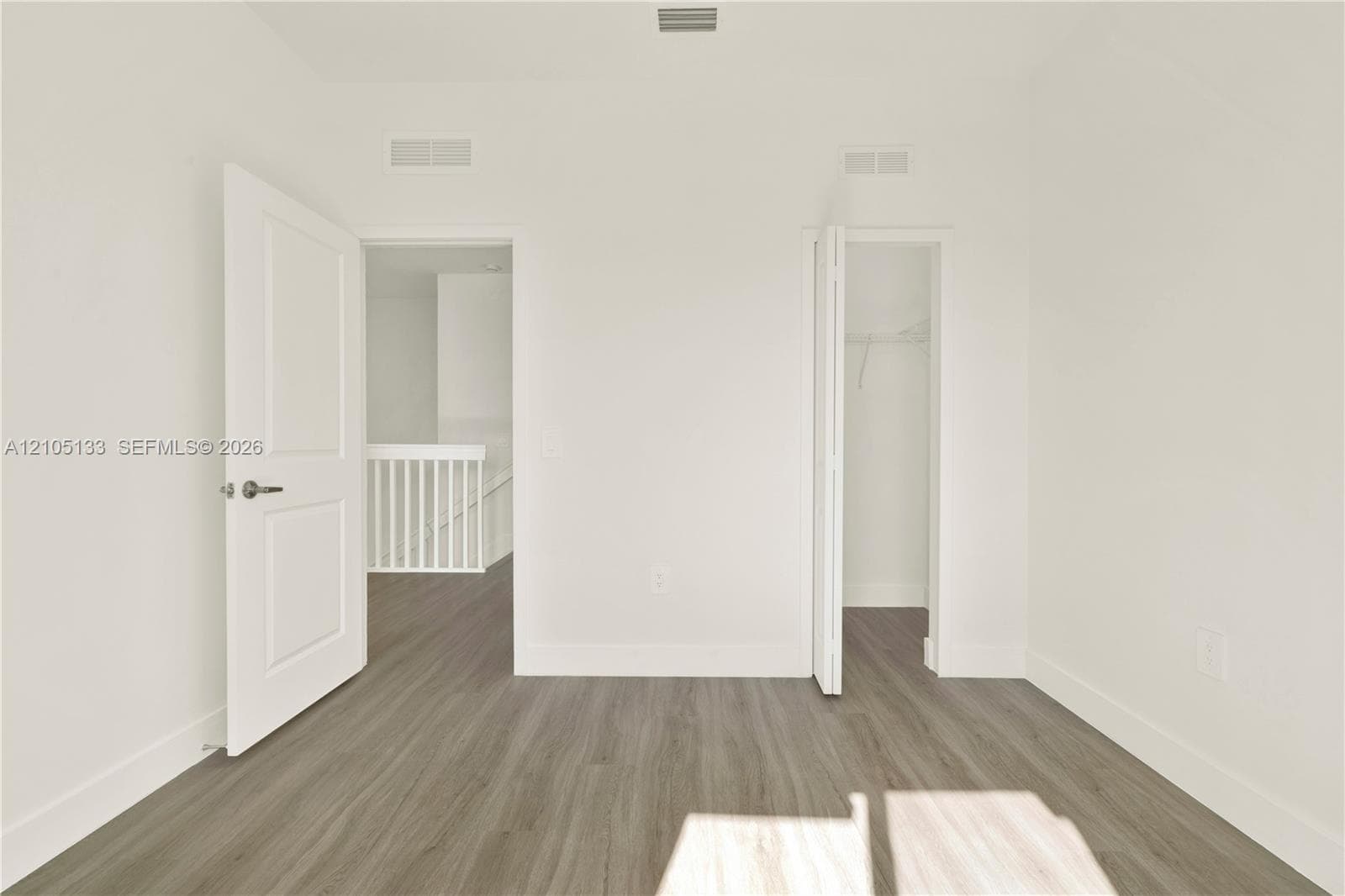 Wood-finish flooring throughout, white walls, and a white interior door with a satin nickel lever handle