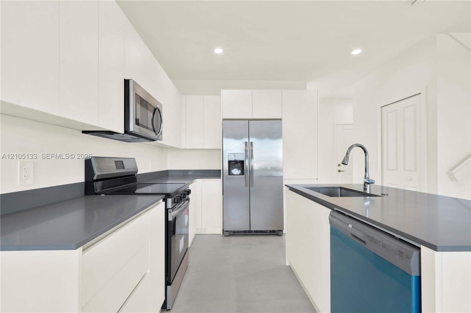 Kitchen featuring white cabinetry, stainless steel appliances, dark countertops, and a kitchen island with an integrated sink