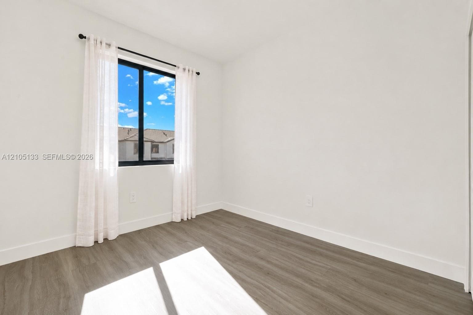 Wood-finish flooring with white baseboards, a large black-framed window, and neutral wall tones