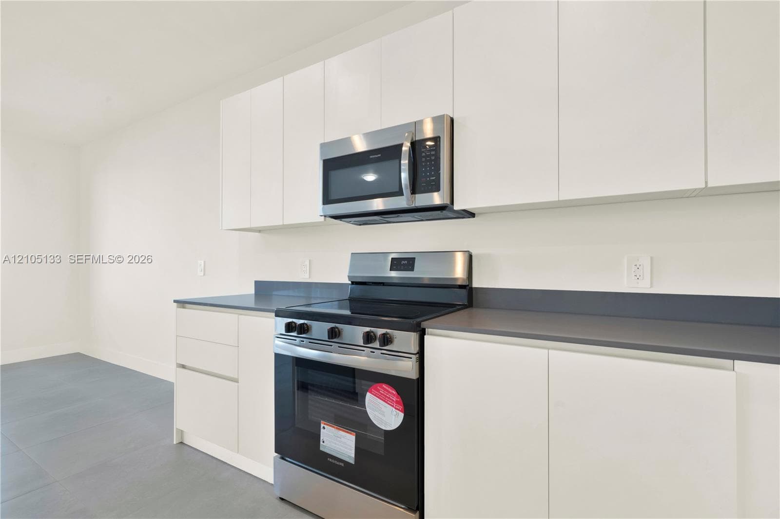 Modern kitchen featuring white flat-panel cabinetry, stainless steel microwave and range, and dark countertops