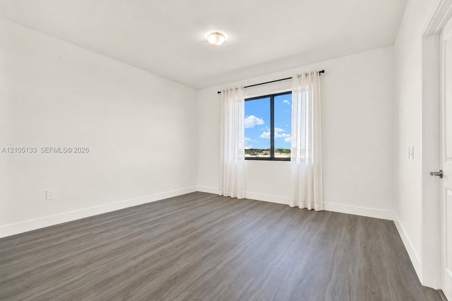 Wood-finish flooring, white walls, and a window with a black frame