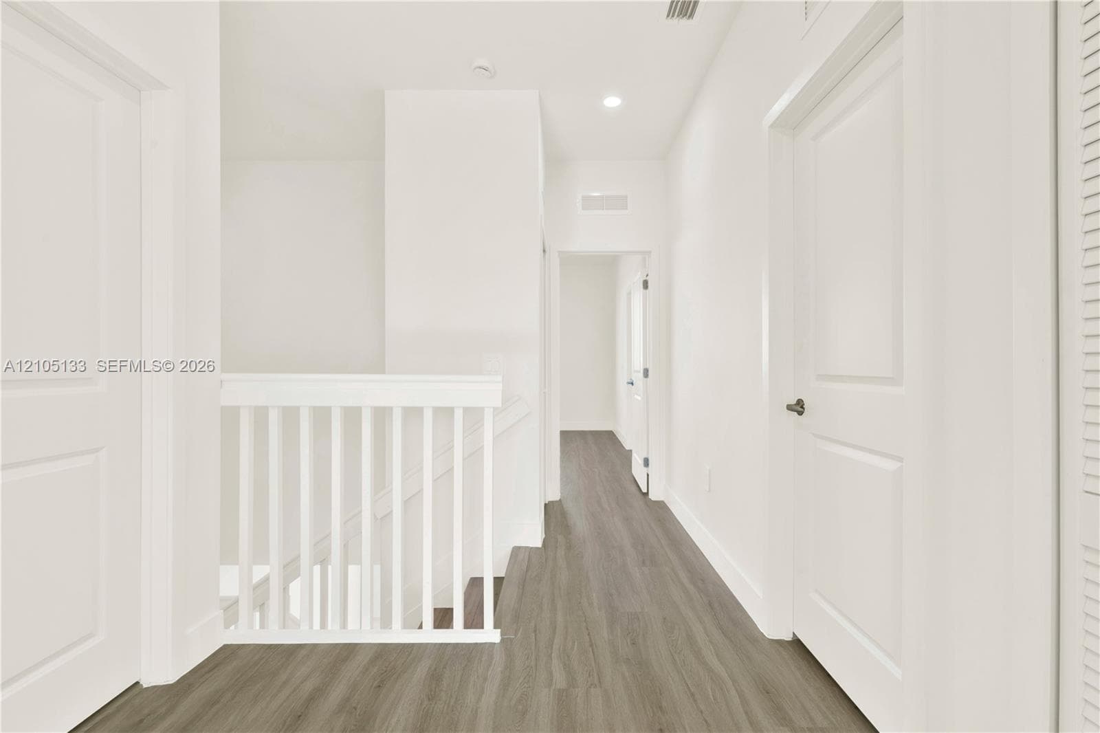 Hallway with wood-finish flooring, white panel doors, recessed lighting, and a white stair railing