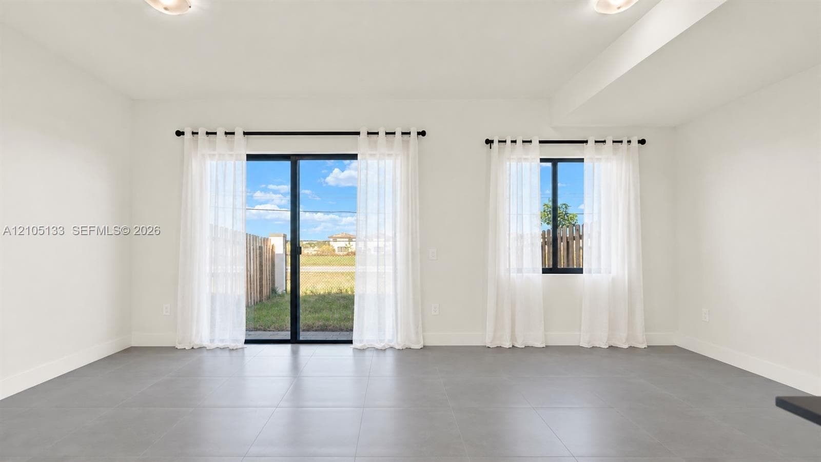 Spacious room featuring neutral tone walls, dark tile flooring, a large sliding glass door, a single pane window, and ceiling-mounted light fixtures