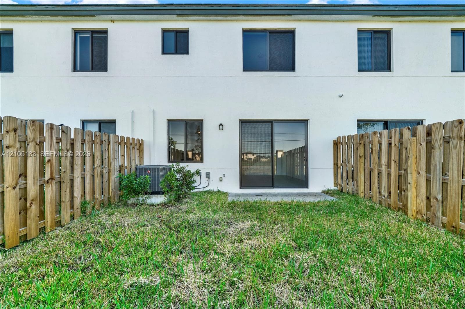 Private backyard with a wood picket fence, concrete patio, and mature lawn