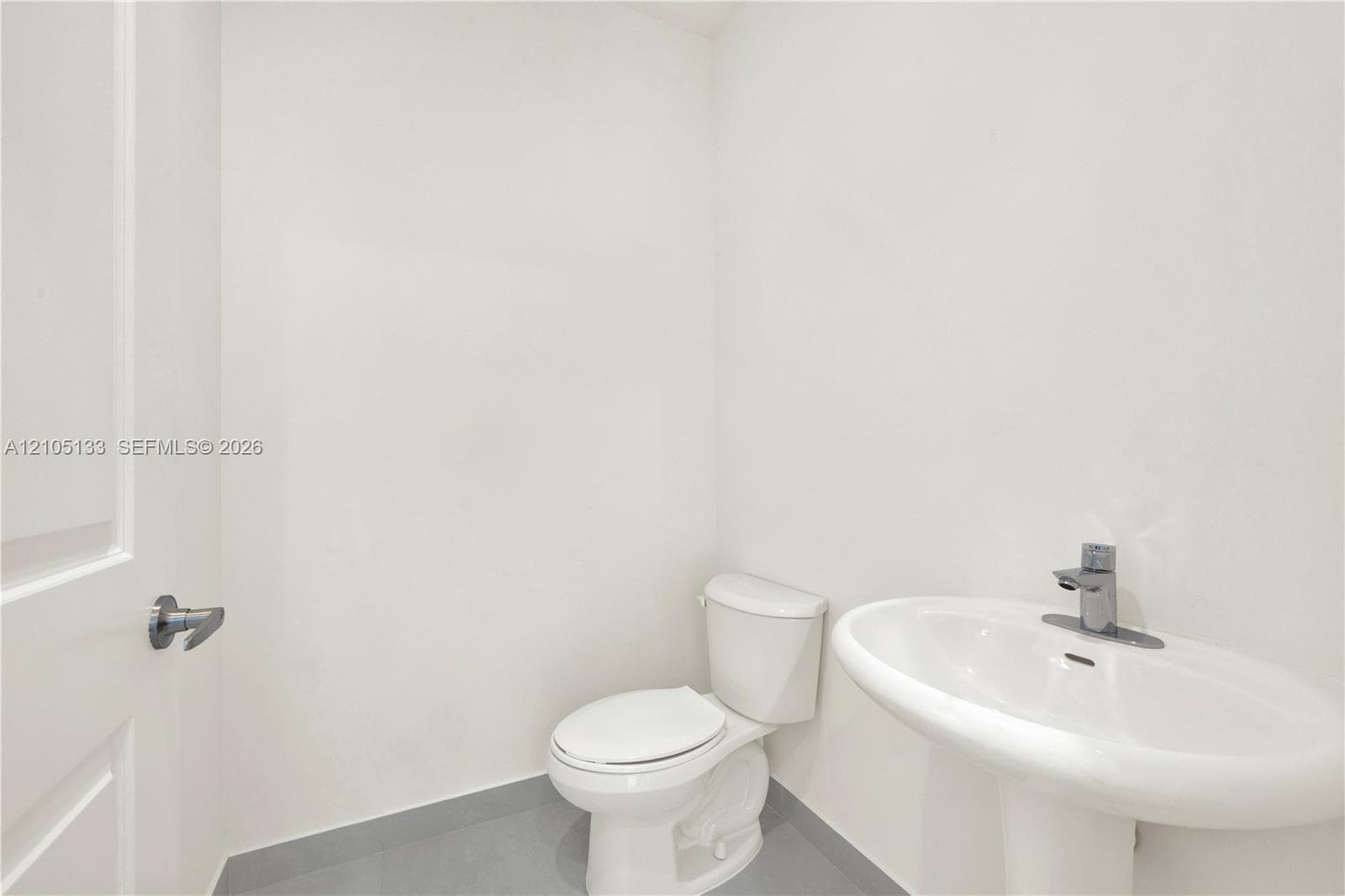 Pedestal sink, chrome single-handle faucet, white toilet, and gray tile flooring
