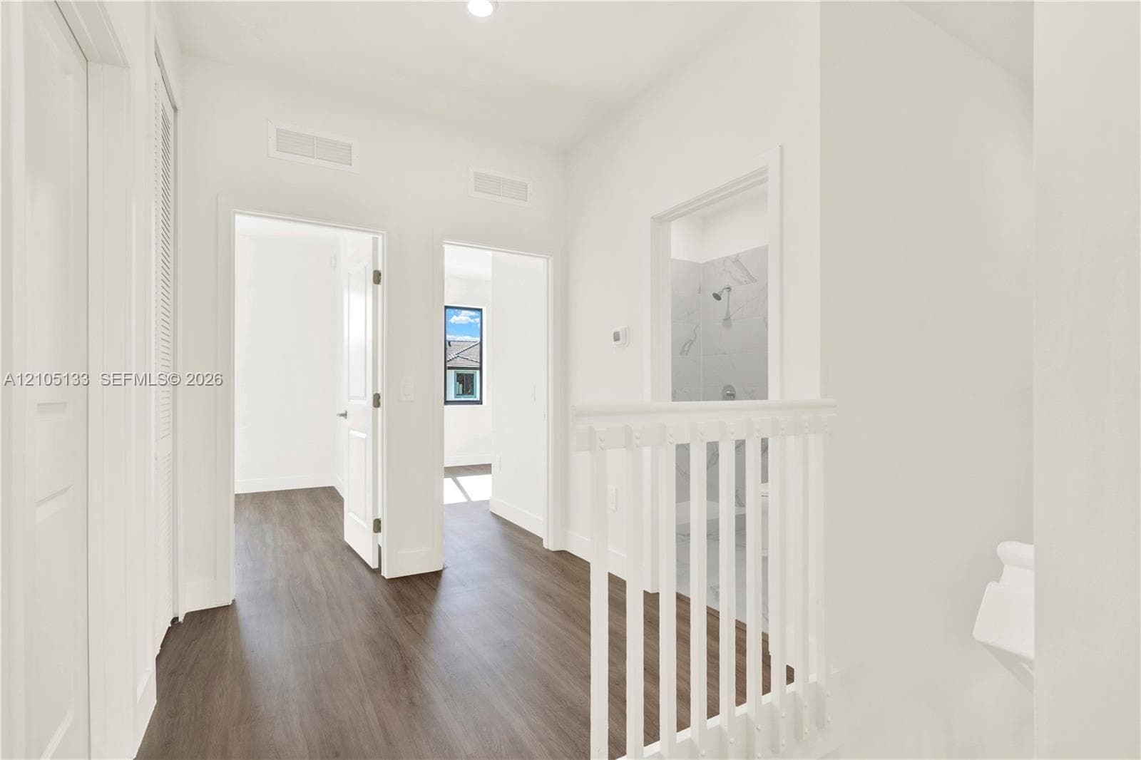 Wood-finish flooring, white walls, white doors, and a white staircase with balusters