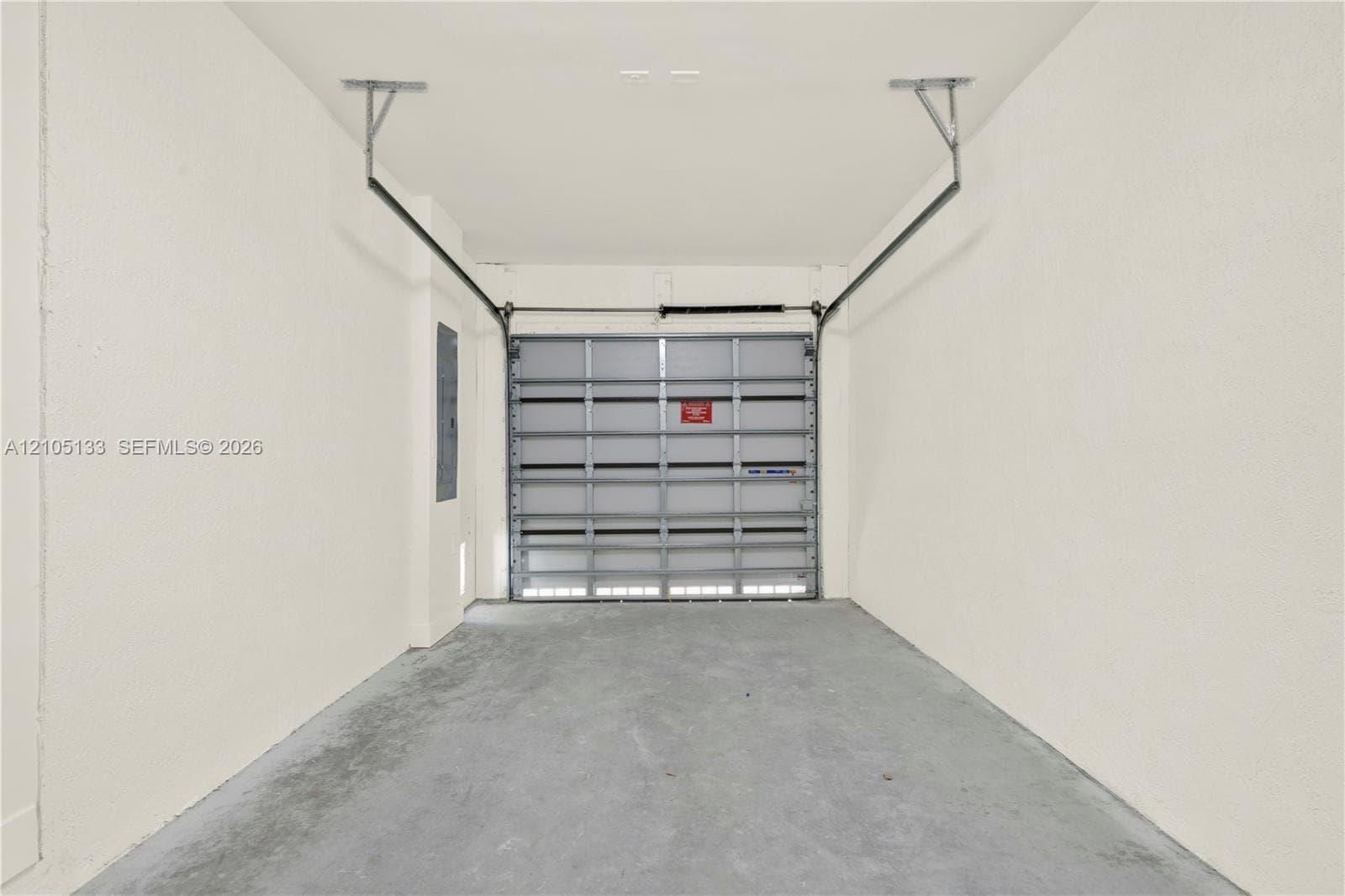 Attached garage with a roll-up door, concrete flooring, and painted walls