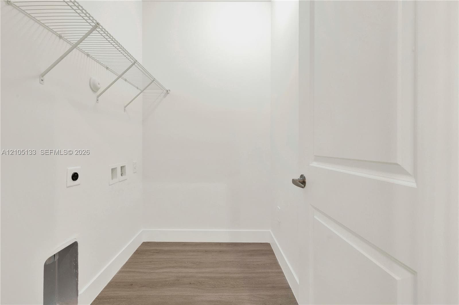 Laundry area featuring a white wire shelf, wood-finish flooring, and a paneled interior door