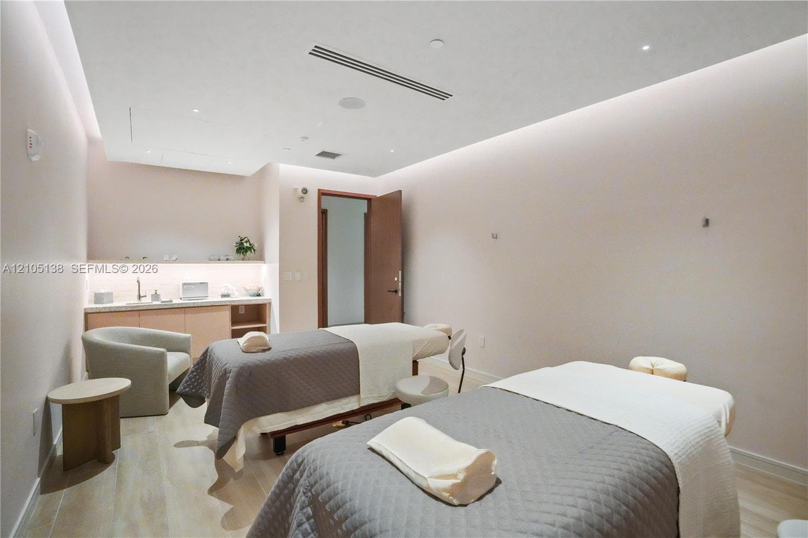 Two treatment tables, recessed ceiling lighting, wood-finish flooring, built-in cabinetry with sink, and a solid core door