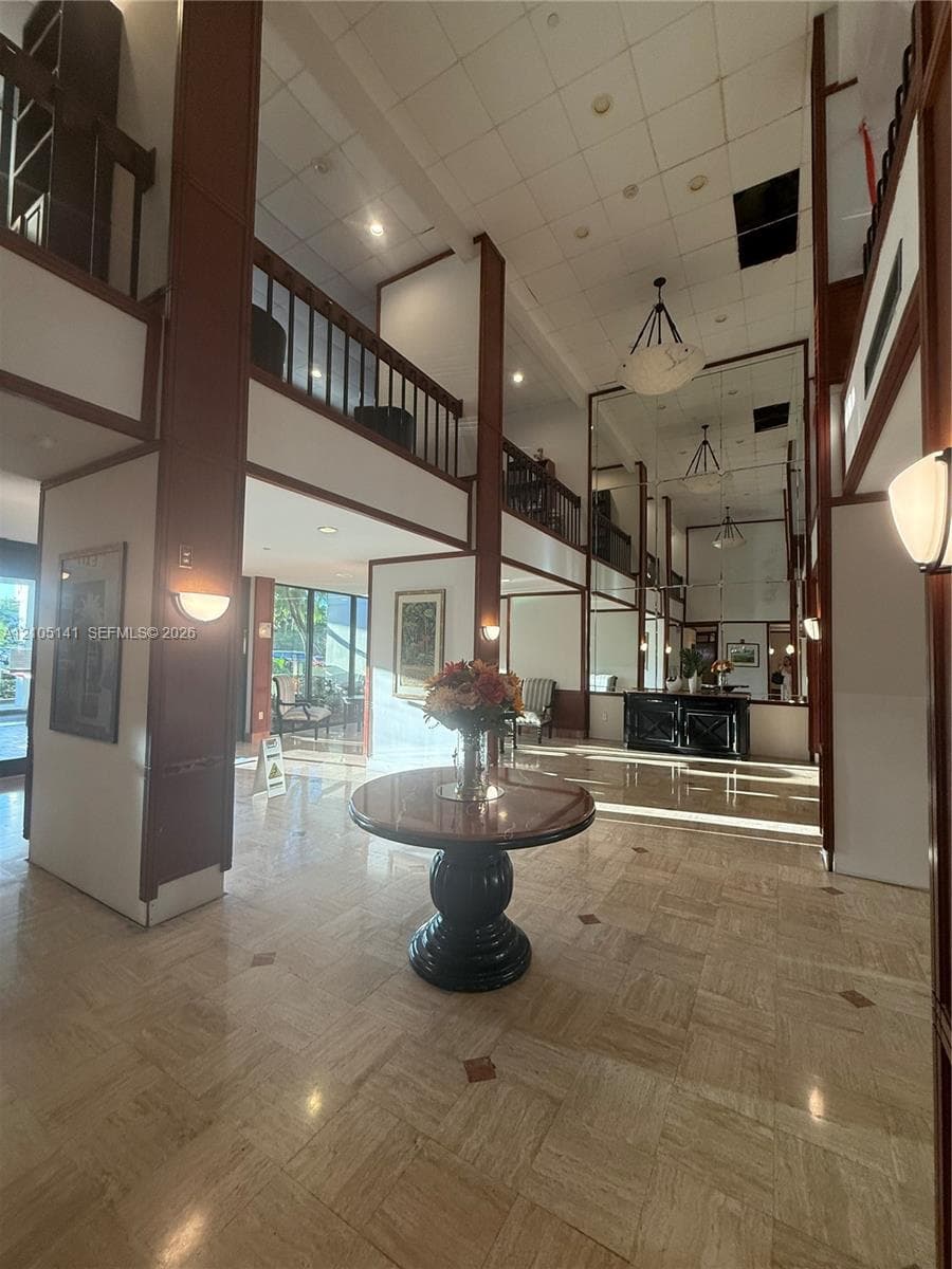 Grand foyer featuring a double-height ceiling, polished stone flooring with inset detailing, custom wood-trim accents, mezzanine level with railing, and full-wall mirror panels