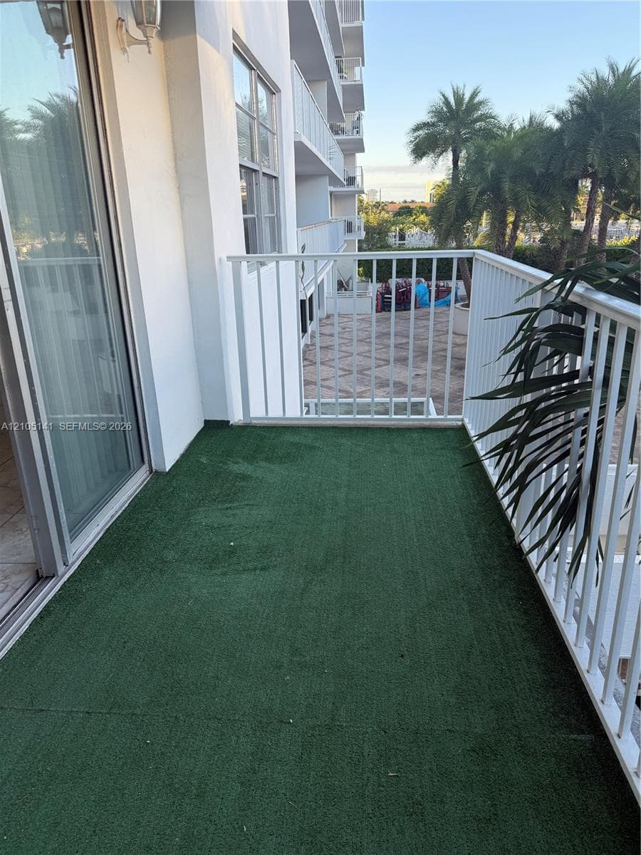Private balcony featuring synthetic turf surfacing and white metal railings, accessible via sliding glass doors