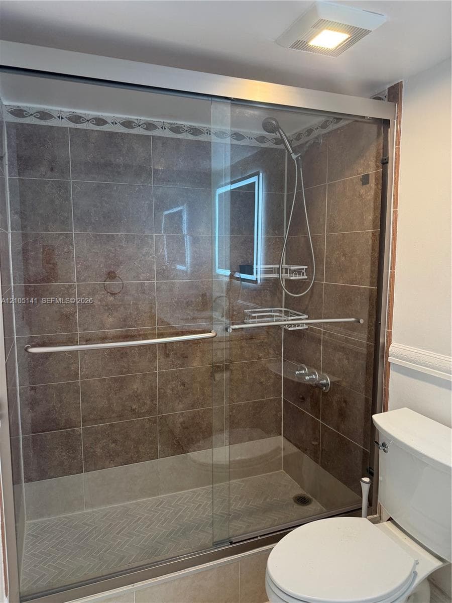 Shower enclosure featuring floor-to-ceiling tiled walls, a decorative tile border, sliding glass doors, and a built-in handheld showerhead
