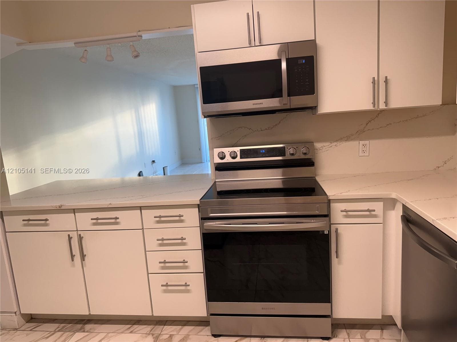 Kitchen featuring white cabinetry, stone-look countertops with vein detailing, and stainless steel appliances including an over-the-range microwave and a slide-in electric range