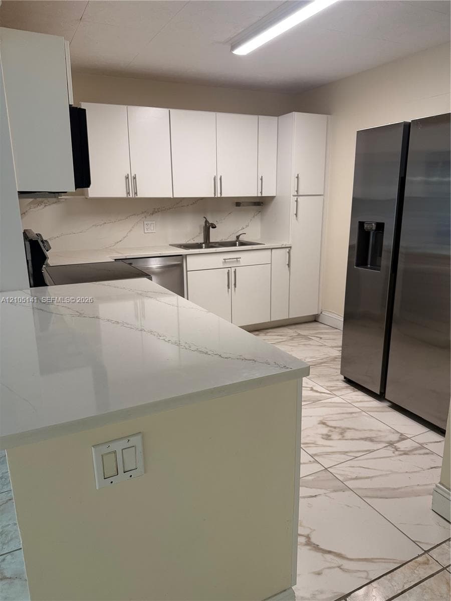 Kitchen featuring white cabinetry, stone-finish countertops with integrated backsplash, stainless steel appliances, and large-format porcelain tile flooring