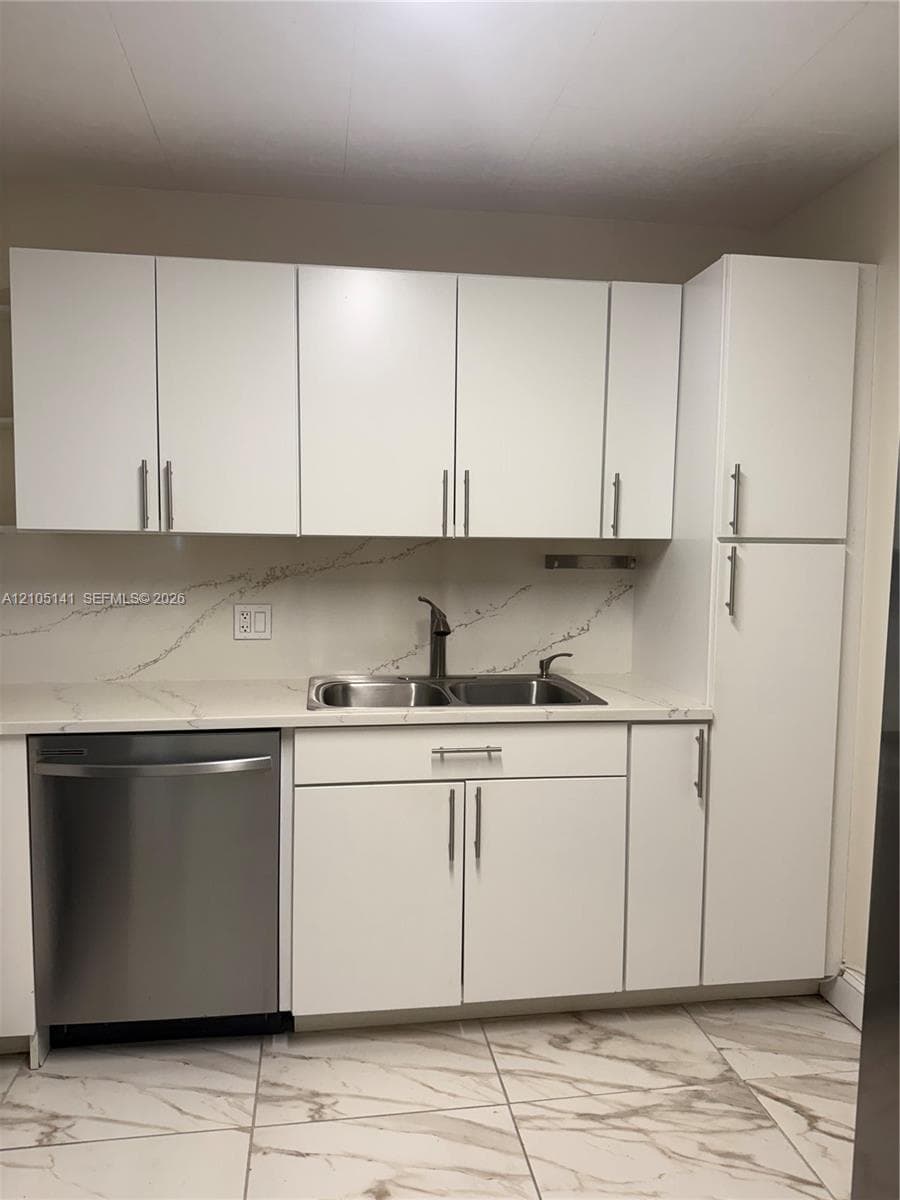 White shaker-style cabinetry, patterned stone-finish countertops, full-height stone-finish backsplash, stainless steel under-mount sink with matte finish faucet, and large-format porcelain tile flooring