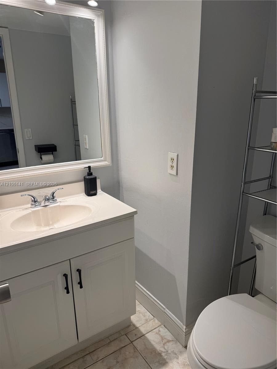 White vanity cabinet featuring matte black hardware, integrated molded sink, wall-mounted framed mirror, and tile flooring