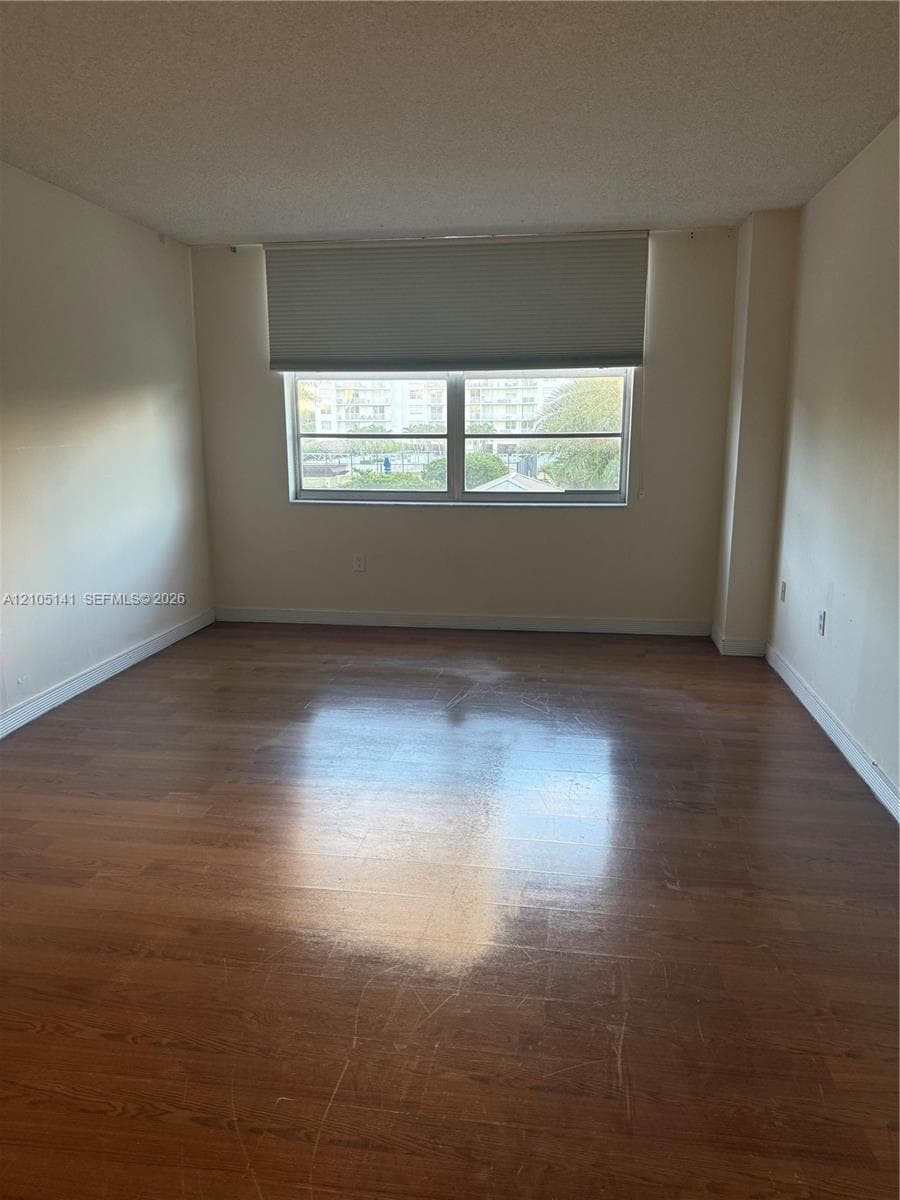 Room featuring wood-finish flooring, neutral-toned walls, and a large horizontal window with a fitted pleated shade