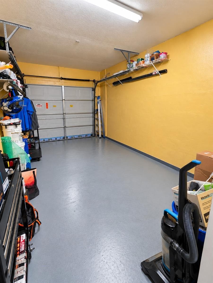 Attached garage featuring a light gray finished floor, overhead lighting, and built-in shelving