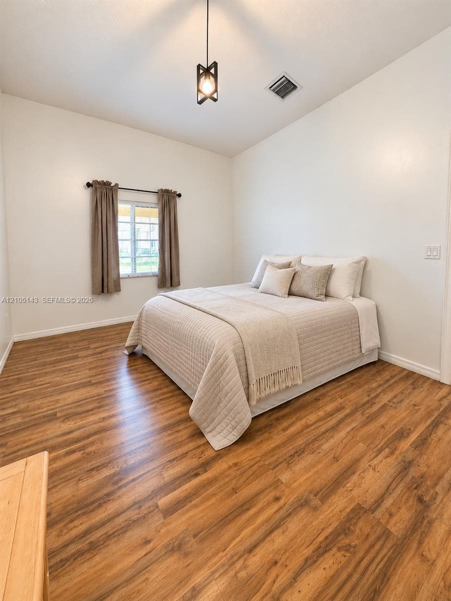 Vaulted ceiling, wood-finish flooring, white walls, and a modern ceiling light fixture