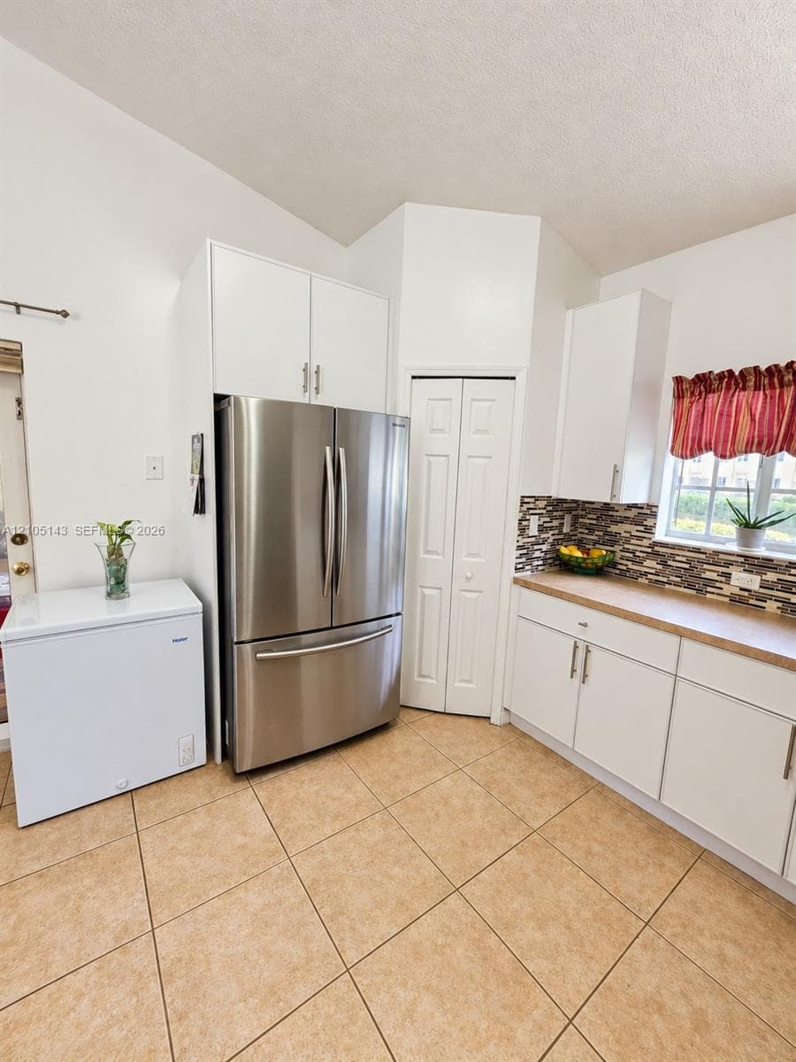 Vaulted ceiling kitchen featuring white cabinetry, stainless steel refrigerator, and tiled flooring
