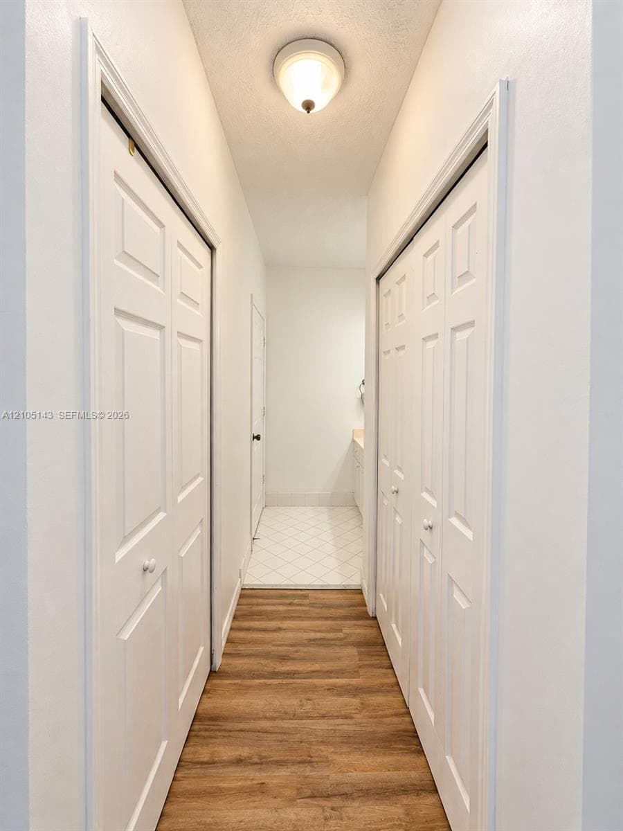 Wood-finish flooring leading to an interior space with white tile flooring and a built-in vanity