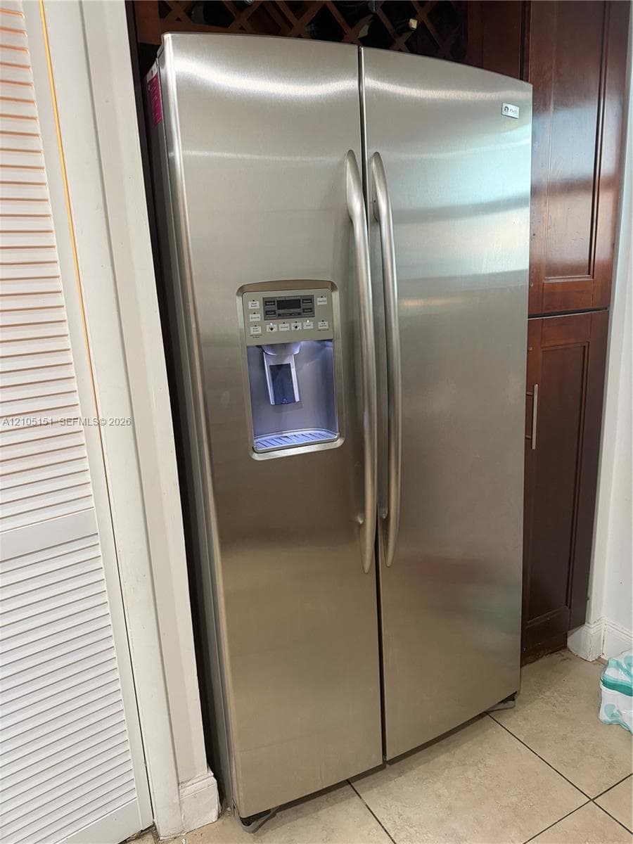 Stainless steel side-by-side refrigerator featuring an external water and ice dispenser, digital temperature interface, and dark wood-finish cabinetry with built-in wine storage