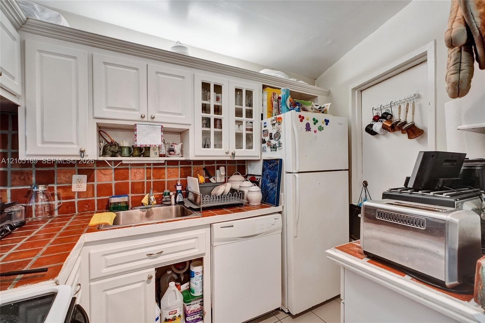 White cabinetry with glass-front accents, stainless steel sink, and a red tile backsplash