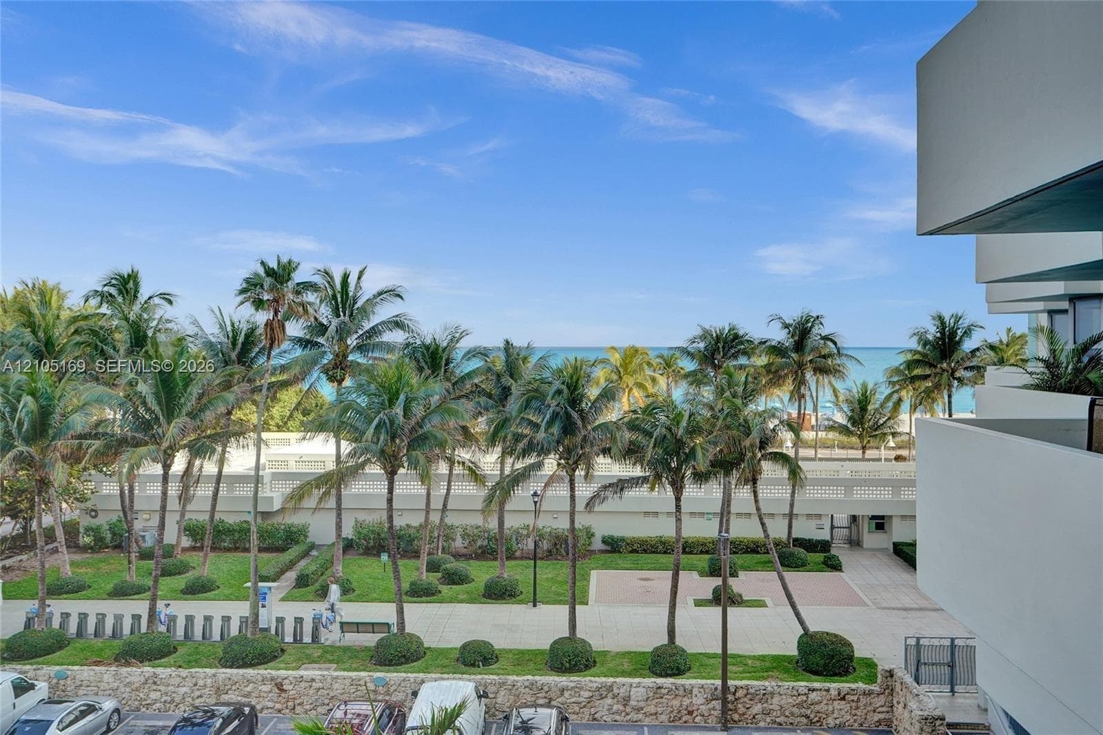 Oceanfront setting featuring extensive palm trees, manicured lawns, and a clear blue sky