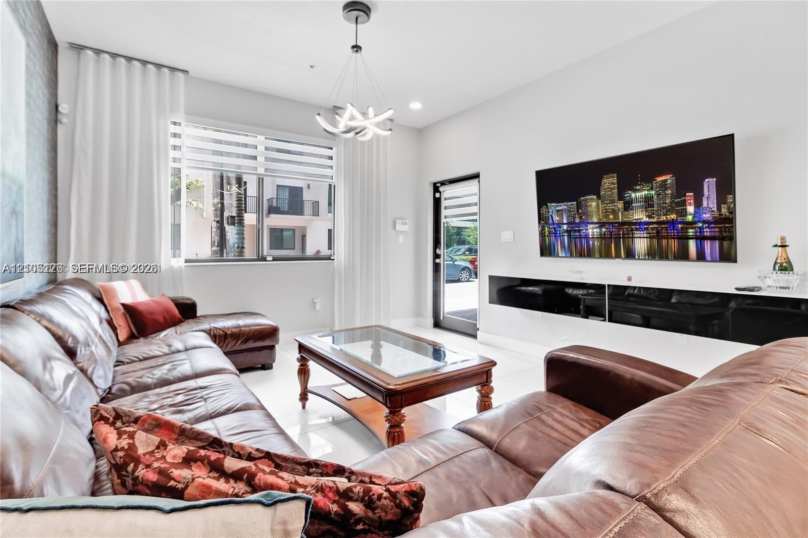 Living area featuring high ceilings, a built-in wall-mounted black media console, large-format tile flooring, a modern multi-arm chandelier, and dual-layered window treatments