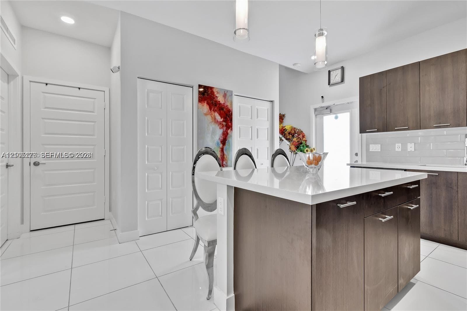 Kitchen featuring a center island with a solid surface countertop, wood-finish cabinetry, white tile flooring, and modern pendant lighting