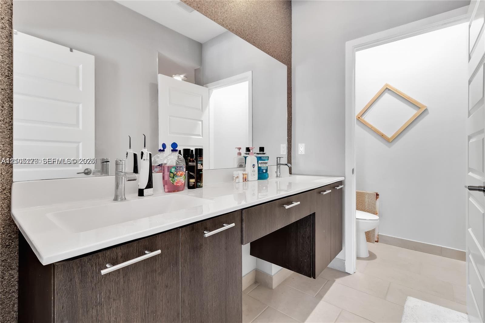 Floating vanity featuring dark wood-finish cabinetry, a wide countertop with dual integrated sinks, polished chrome fixtures, and a wall-to-wall mirror