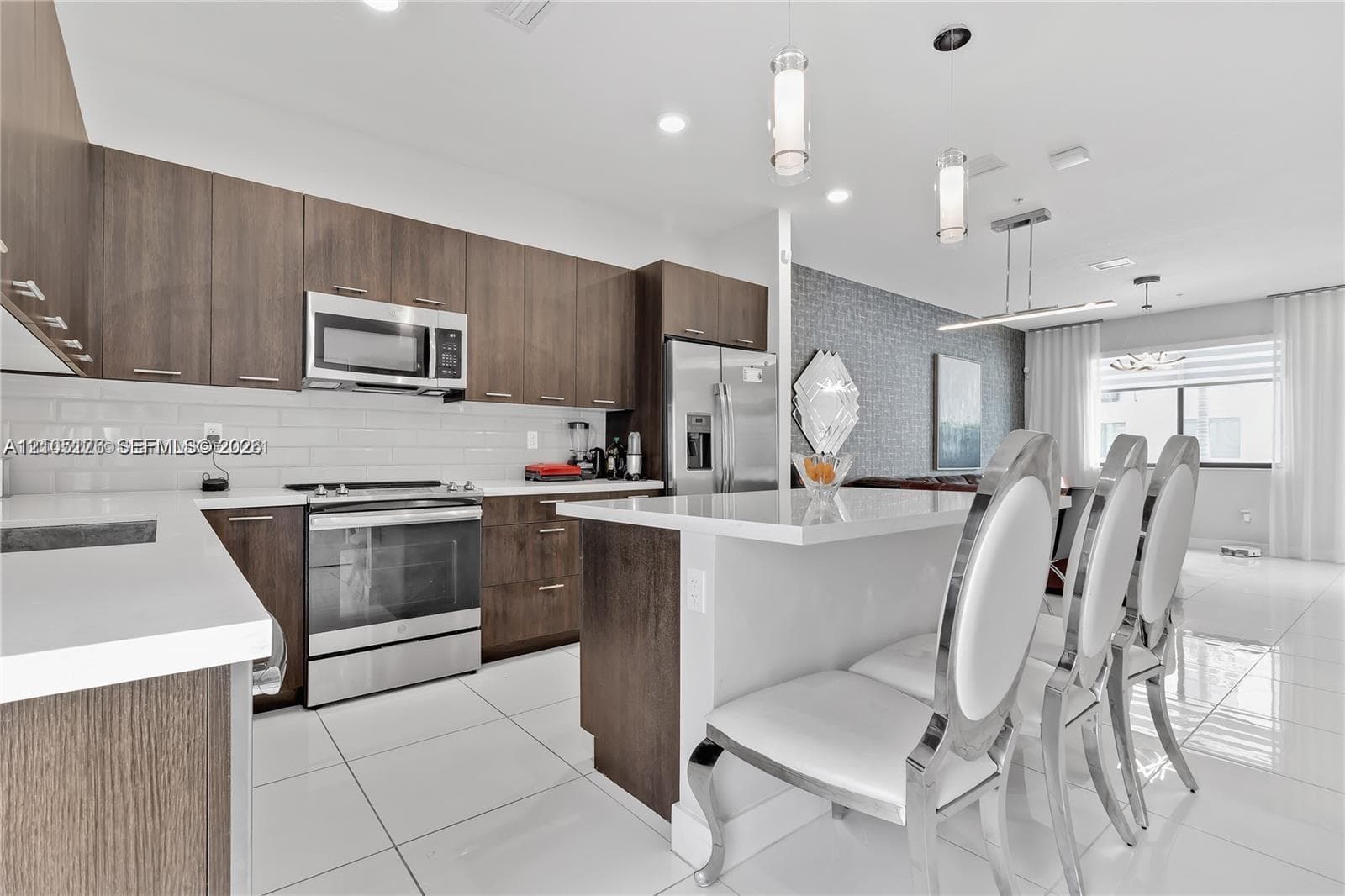 Kitchen featuring flat-panel wood-finish cabinetry, white solid-surface countertops, subway tile backsplash, stainless steel appliances, and a central island with pendant lighting