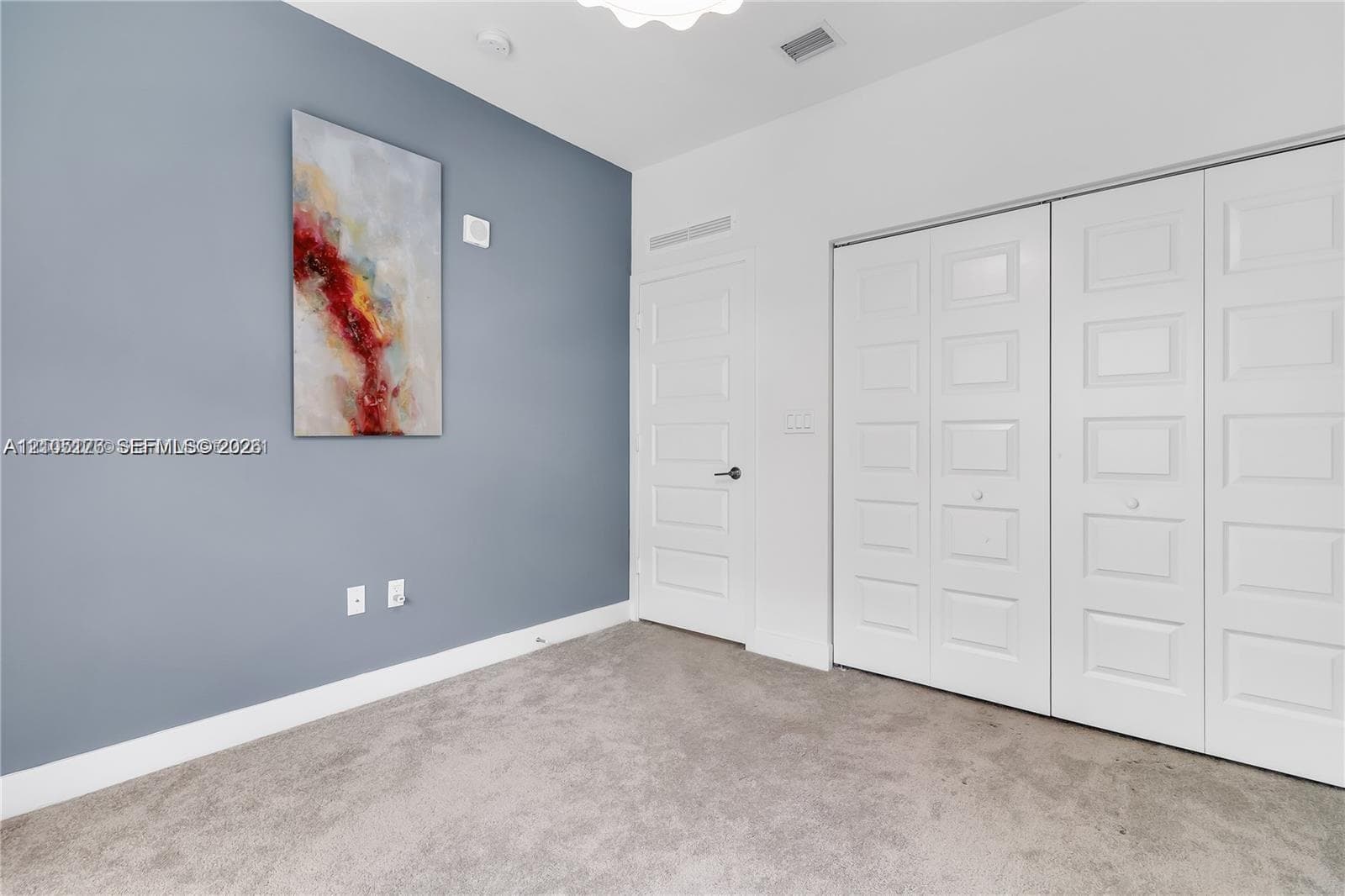 Room featuring wall-to-wall carpeting, a blue accent wall, neutral interior paint, a solid-core single door, and double bi-fold closet doors